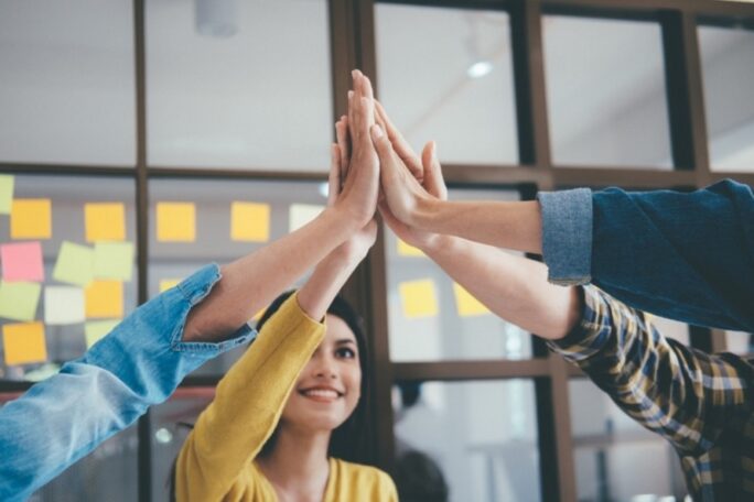 Four people high fiving each other in a conference room
